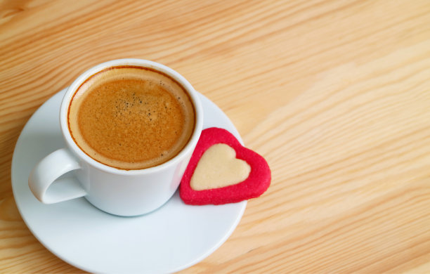 一杯热咖啡和一个心形饼干放在木桌上图片下载