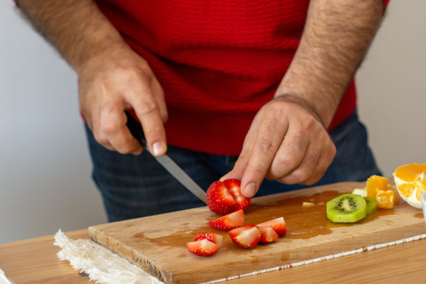 穿着红色衬衫的男人在阁楼厨房烹饪美味健康的食物。准备水果沙拉。垂直的照片。美食摄影概念。图片下载