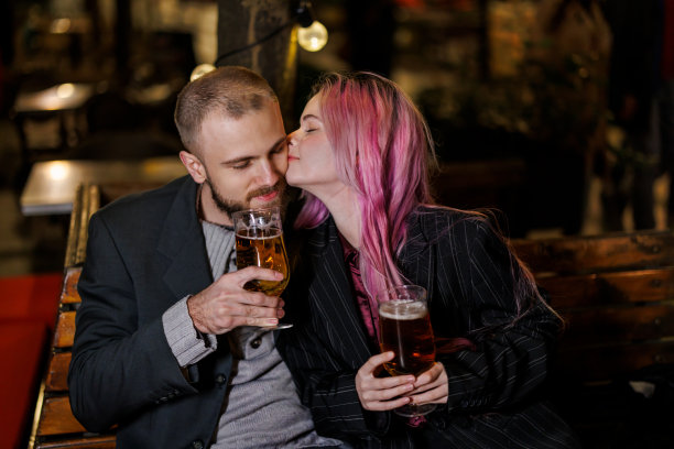 一个英俊的年轻人和他美丽的女朋友晚上坐在一家餐馆里，喝着啤酒，享受着爱情。图片下载