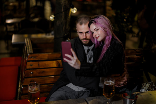 一对美丽时尚的情侣正坐在一家餐厅里喝着啤酒，自拍。图片下载