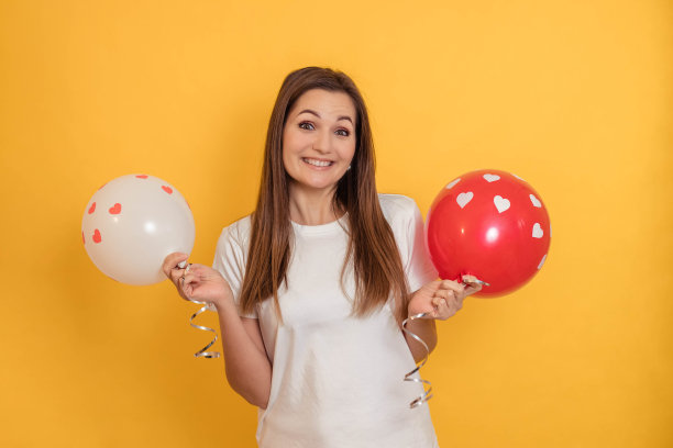 有趣的肖像，一个漂亮的女孩在黄色的背景与白色和红色的气球在她的手中图片下载