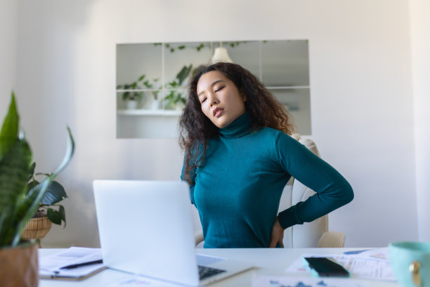 年轻的亚洲女性坐在笔记本电脑前的家庭办公桌前，用痛苦的表情触摸疼痛的背部，在笔记本电脑上工作后遭受背痛的痛苦图片下载