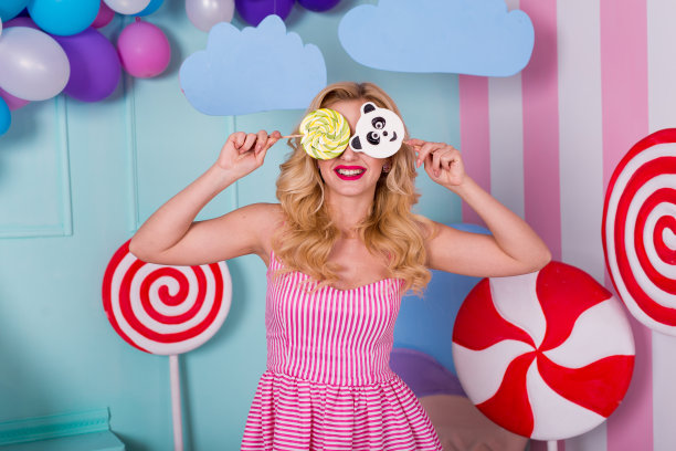 令人惊叹的爱吃甜食的女人的肖像，她穿着粉红色的裙子，拿着糖果，在背景上摆姿势，装饰着巨大的冰淇淋。棒棒糖的熊猫图片下载