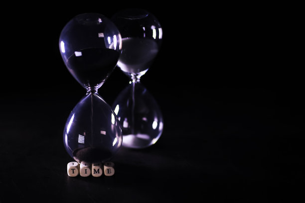 沙子穿过沙漏的灯泡，在截止日期的倒计时中测量流逝的时间，在深色的桌子背景上有复制空间。图片下载