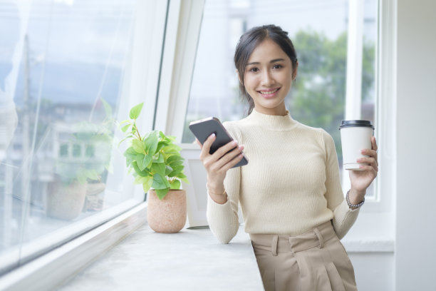 迷人的女人在明亮的现代办公室，使用智能手机。图片下载