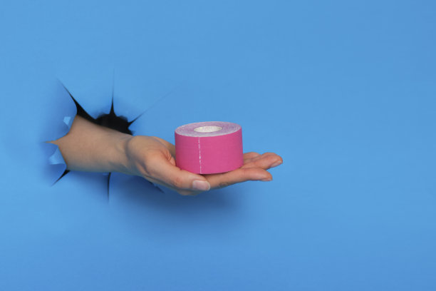 手上有蓝色背景的粉色人体运动学胶带。物理治疗和治疗手腕疼痛，疼痛和紧张胶带。弹性治疗带。图片下载