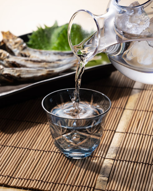 清酒倒在一个多面玻璃杯里，烤沙丁鱼放在后面。图片下载