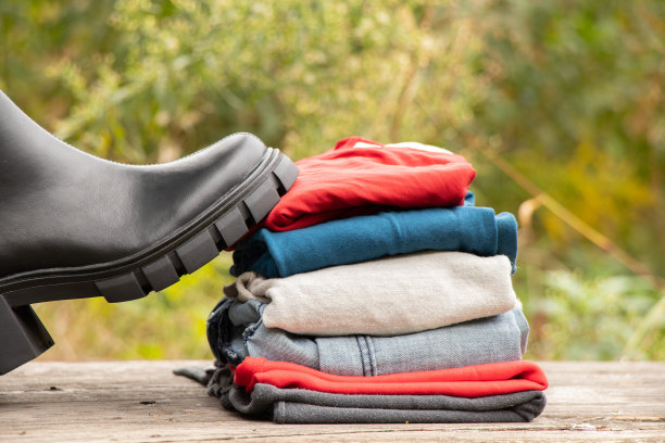 女式厚底黑高筒靴和一堆东西站在木板上晒太阳，女式鞋子和冬装，时髦的衣服和鞋子图片下载