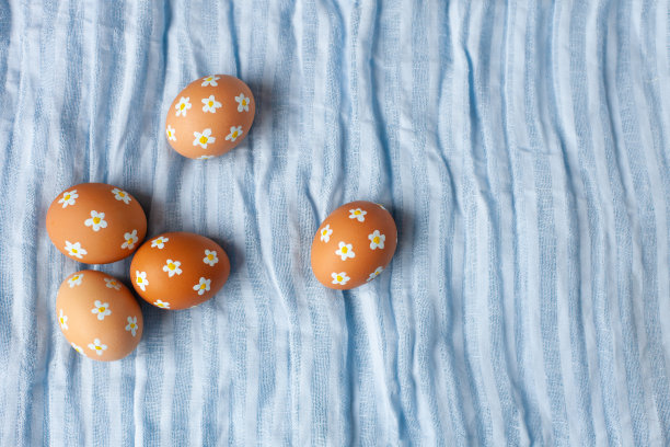 蓝色亚麻面料上绘有小花的自然色复活节彩蛋。图片下载