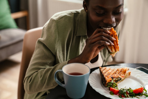年轻美丽的微笑的非洲女人与辫子的头发吃三明治图片下载