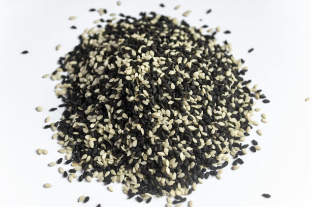 黑色和白色的芝麻躺在滑梯上。桌上有混合的白芝麻和黑芝麻。白色背景上是一座芝麻山。图片下载