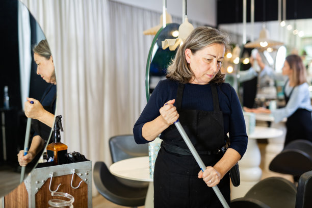 老年女理发师在现代理发店扫地图片下载