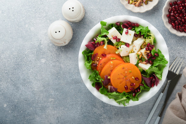 沙拉。新鲜蔬菜沙拉配羊乳酪，柿子，石榴和开心果，白盘子。健康美味的冬季圣诞沙拉。健康均衡的饮食。前视图。图片下载