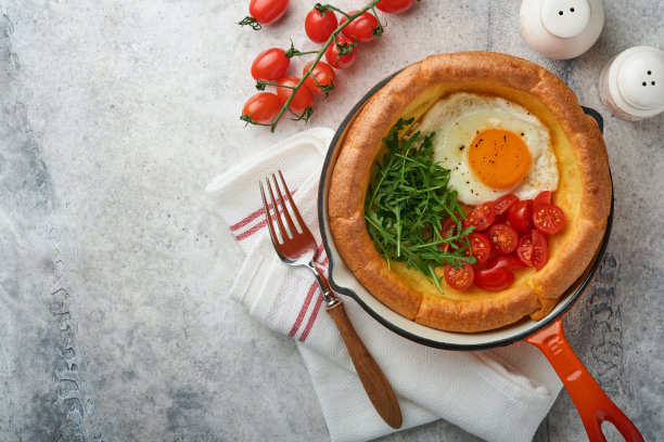 荷兰婴儿煎饼。新鲜自制荷兰婴儿煎饼煎蛋，西红柿和绿色芝麻菜在芦苇铸铁锅浅灰色混凝土质朴的桌子上。平躺，靠近点。图片下载