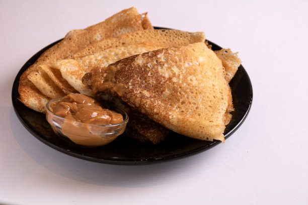 照片煎好的薄煎饼和煮好的炼乳堆在一个小碗里躺在盘子上图片下载