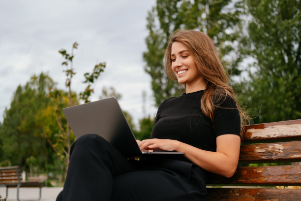 微笑的金发女子喜欢坐在长椅上的笔记本电脑工作。图片下载