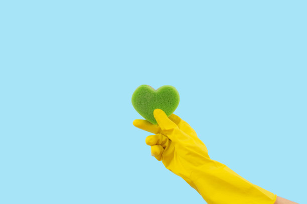 心形绿色海绵和黄色橡胶手套在蓝色背景。极具创意的清洁服务概念。图片下载