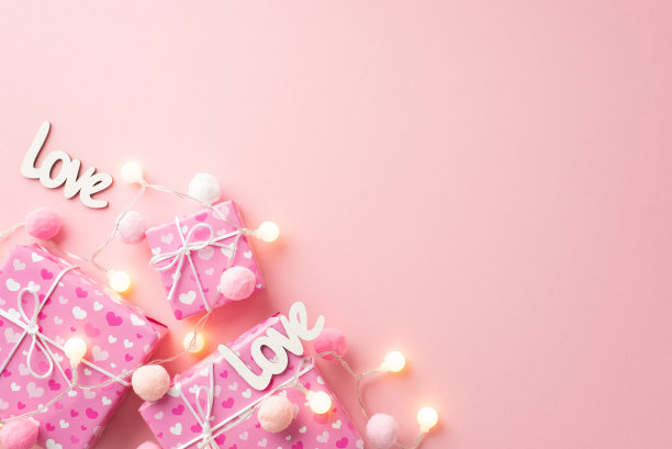 情人节的概念。顶视图照片的礼物盒灯泡花环铭文爱和蓬松的绒球在孤立的粉彩粉红色背景与复制空间图片下载