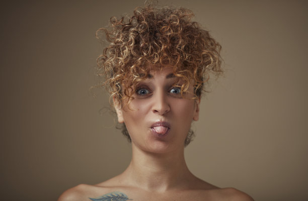 画像的年轻女子卷发伸出舌头在相机。图片下载