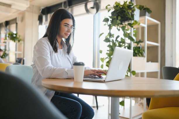 微笑的女孩学生与skype老师在线学习，快乐的年轻女子学习语言听讲座看网络研讨会写笔记看笔记本电脑坐在咖啡馆，远程教育图片下载