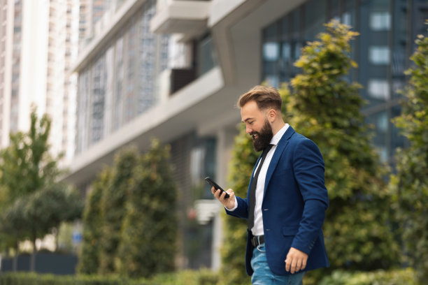 微笑的白人商人在户外散步时使用智能手机。图片下载