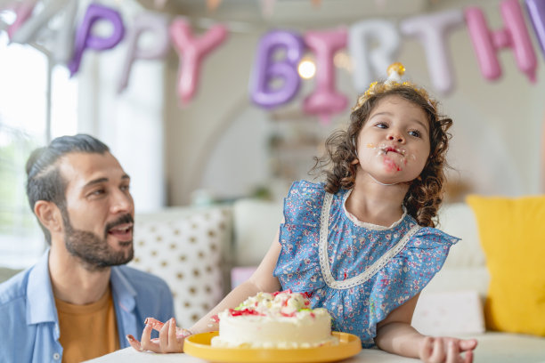 幸福的单身爸爸和女儿一起在家里的客厅享受吹生日蛋糕的乐趣和快乐的派对时刻，爸爸和女儿一起在家里度过派对时间图片下载