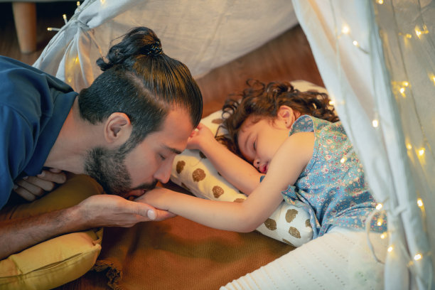 可爱的概念，多种族父母温柔地亲吻他们快乐的小女儿，而她的女儿在玩了一整天后躺在地板上睡着了，照顾温柔，家庭关系爱幸福图片下载