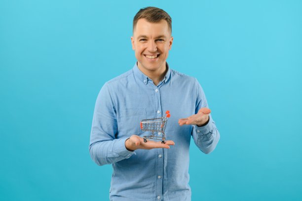 微笑的男子手持迷你购物篮在蓝色背景的肖像。增加销售的概念。图片下载