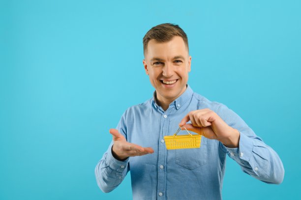 微笑的男子手持迷你购物篮在蓝色背景的肖像。增加销售的概念。图片下载