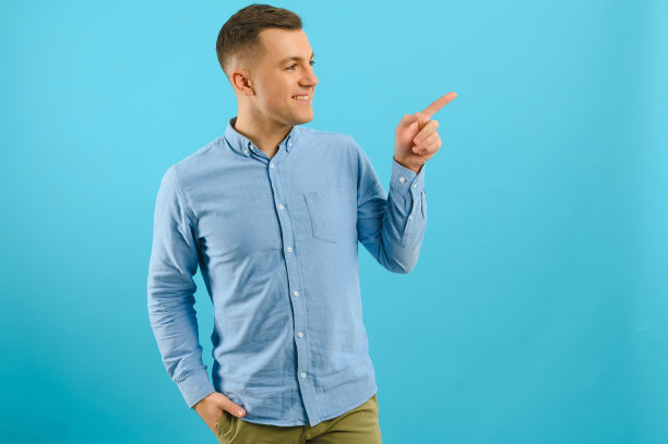 快乐微笑的帅哥穿着衣服，显示复制空间，视觉想象或什么的，或按虚拟按钮，水海洋蓝的颜色背景。图片下载
