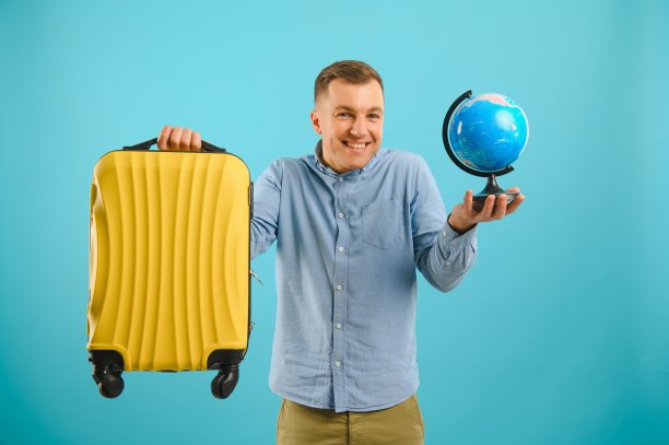 愉快的旅行者游客男子在休闲服装行李箱孤立在蓝色背景。周末出国旅行的男性乘客。航空旅行概念把握全球图片下载