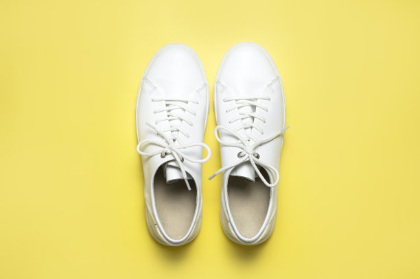 白色运动鞋在黄色背景顶部视图平铺。时尚青春女皮鞋，运动鞋，真皮鞋。简约的鞋店广告时尚风格的鞋子背景图片下载