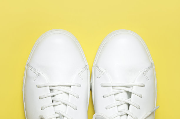 白色运动鞋在黄色背景顶部视图平铺。时尚青春女皮鞋，运动鞋，真皮鞋。简约的鞋店广告时尚风格的鞋子背景图片下载