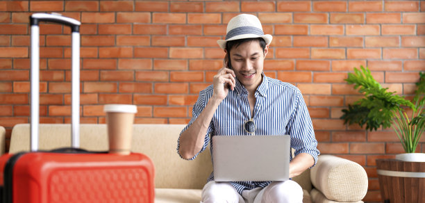 亚洲男子数字游牧民手拿笔记本电脑在酒店大堂等待航班时刻表，准备旅行亚洲男子游客微笑愉快坐在酒店大堂的沙发上图片下载