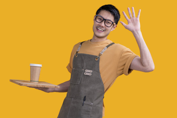 聪明友好的亚洲男眼镜咖啡师小咖啡店老板在围裙的手势欢迎顾客来享受他的咖啡饮料，快乐的亚洲男展示咖啡与微笑和自信的工作室拍摄图片下载