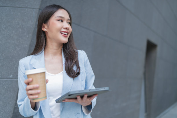 聪明休闲的商务女性女性正式布手拿咖啡杯，一边在平板电脑上查看工作项目时间表，一边走在写字楼走廊，微笑开朗的亚洲女性走在户外图片下载