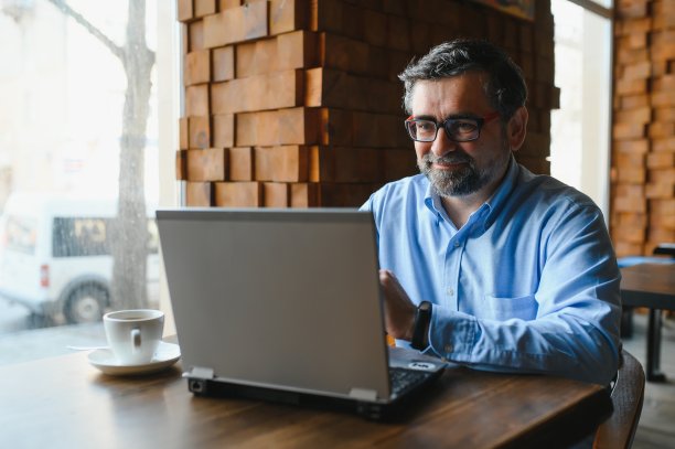 老年男性自由职业者在咖啡馆的笔记本电脑上工作。远程工作的概念。图片下载