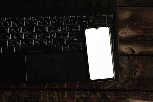 桌上的黑色笔记本电脑上放着一台白色屏幕的手机，这是一个带屏幕的手机模板图片下载