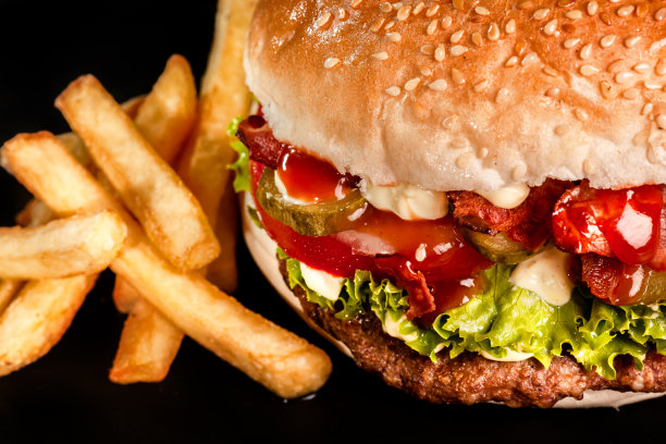 培根汉堡，洋葱，西红柿，黄瓜，生菜和薯条。快餐垃圾食品照片。图片下载
