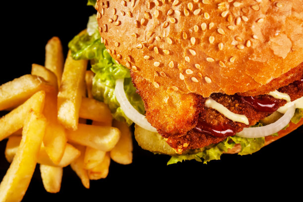 双层炸鸡汉堡配炸薯条，洋葱，黄瓜和生菜。在深色背景上。抽象的照片。图片下载