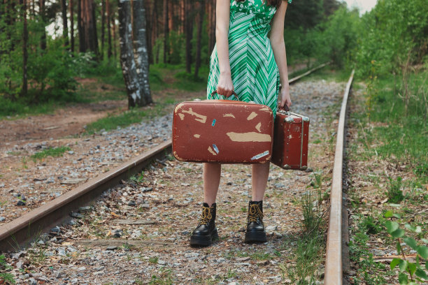 靠近女人在时尚的复古形象与复古行李箱站在铁路在夏季林地，等待。在森林里穿着绿色衣服的时尚年轻女士。旅游度假概念。复制文本空格图片下载