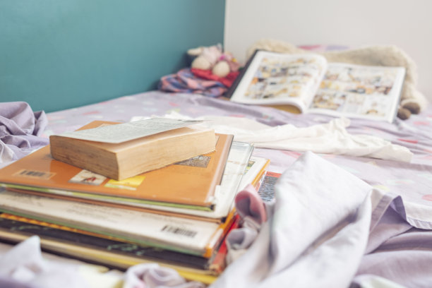 室内生活:一个凌乱的女孩的床的水平日光特写，床单上散落着书。图片下载