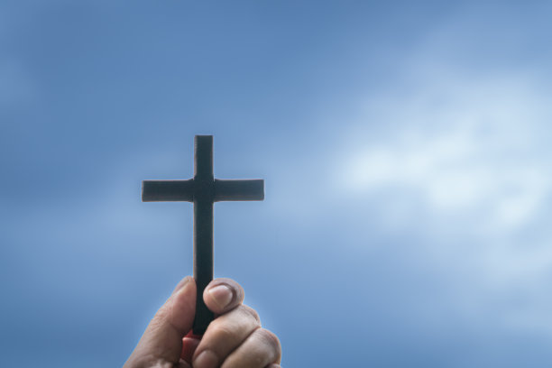 手拿着一个木制的十字架，背景是蓝色多云的天空。图片下载