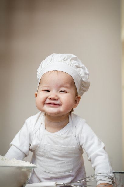 一个亚洲婴儿戴着厨师帽，围着围裙，抹上面粉，准备圣诞姜饼图片下载