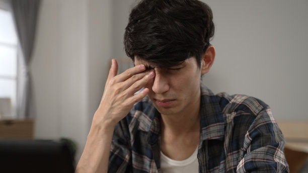 特写:一个疲惫的亚裔中国大学生眼睛模糊，在卧室里学习时揉眼睛，眯着眼睛看电脑屏幕图片下载