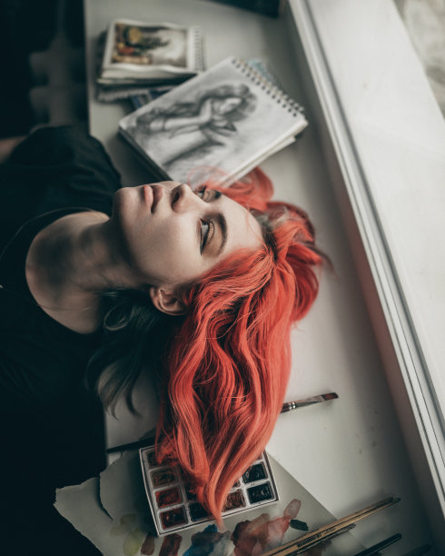 年轻的红发女艺术家正躺在窗户上，手里拿着她的画和颜料图片下载