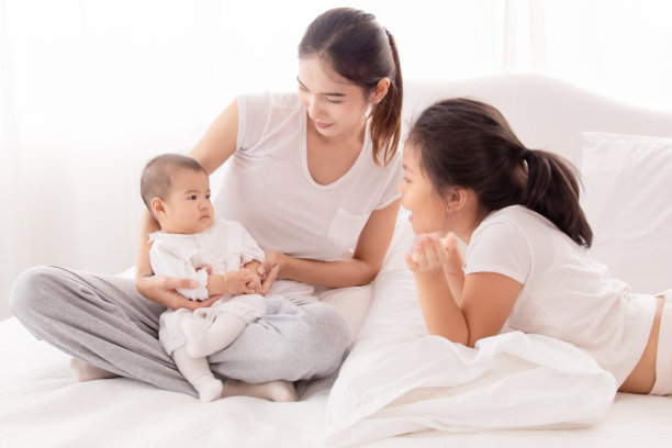 年长的亚洲姐姐在白色房间的床上和新生儿玩耍，美丽的母亲抱着可爱的婴儿，看起来充满了爱和关怀。幸福家庭理念。图片下载