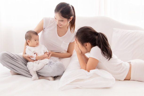 年长的亚洲姐姐在白色房间的床上和新生儿玩耍，美丽的母亲抱着可爱的婴儿，看起来充满了爱和关怀。幸福家庭理念。图片下载