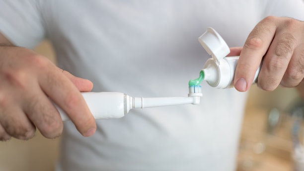 白人的手往电动牙刷里倒牙膏。图片下载