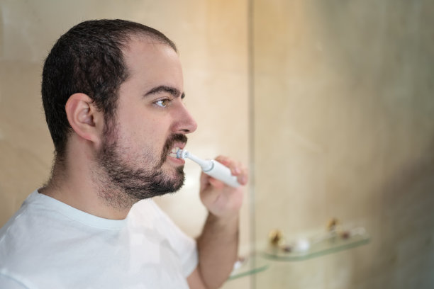 年轻的白人男子一边刷牙一边看着浴室的镜子，复印空间。图片下载